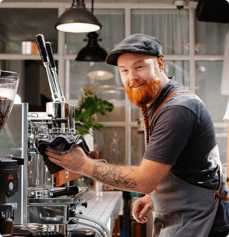 Bearded barista in a cap and apron operating an espresso machine