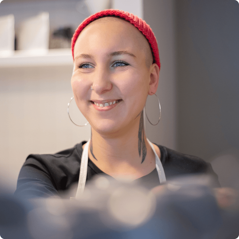 Smiling staff member in a red beanie and dark apron
