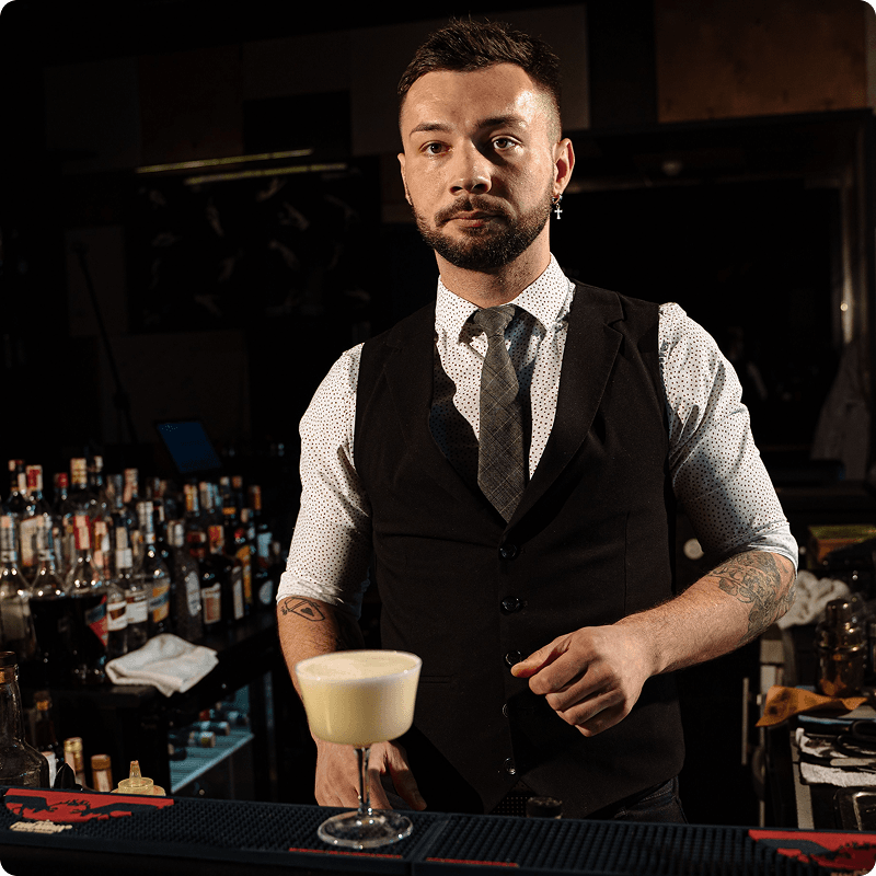 Bartender in a waistcoat and tie standing behind the bar with a cocktail