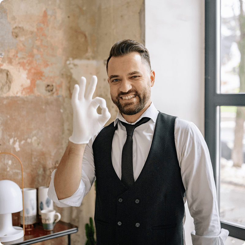Waiter in a waistcoat and tie giving an OK sign with a gloved hand